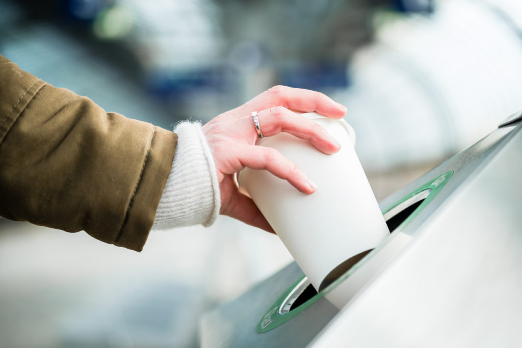 Woman using waste separation container throwing away disposable paper coffee cup