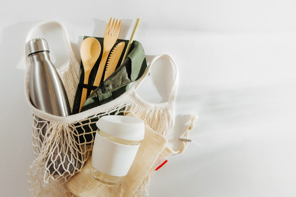 Mesh market bag with bamboo cutlery, reusable coffee mug and water bottle. Sustainable lifestyle. Plastic free concept.