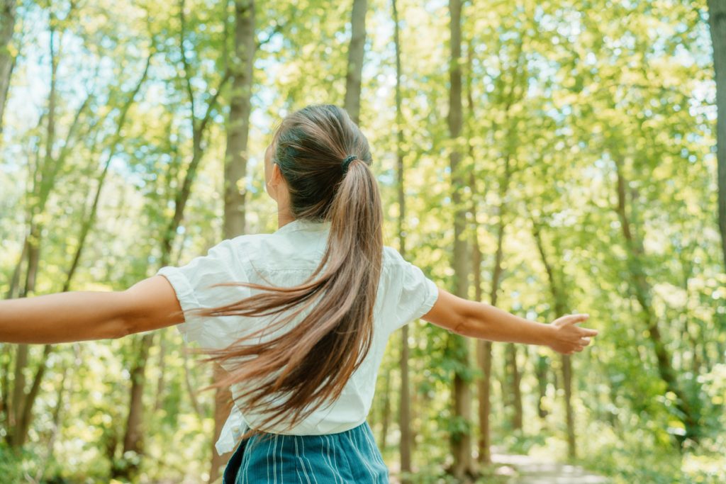 Happy woman in forest with open arms from behind breathing clean air. Environment, no pollution healthy natural living lifestyle.